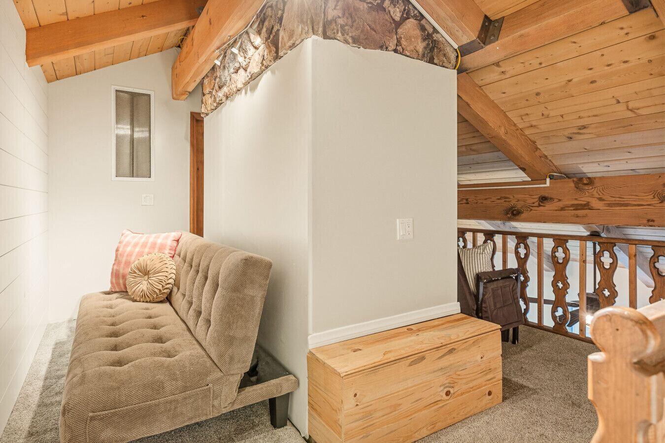 Une chambre aménagée en mezzanine avec un canapé-lit, une commode en bois et un balcon doté d’une balustrade.