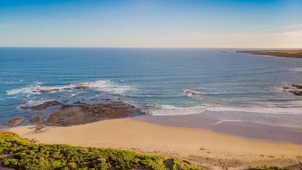 Un paysage côtier avec une plage de sable, des affleurements rocheux et une vue dégagée sur l’océan.
