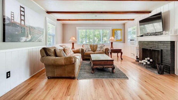 Un salon spacieux doté de parquets en bois, d’une cheminée et d’un grand téléviseur.