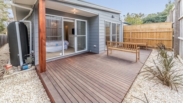 Una casa moderna con un patio, un deslizador de vidrio que da a un dormitorio y una terraza de madera.