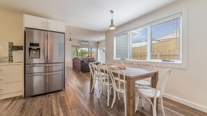Una cocina moderna con un refrigerador de acero inoxidable, dispensador de agua integrado y un comedor con mesa de madera y sillas blancas.