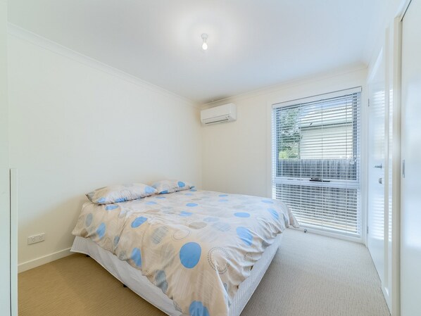 Un dormitorio con cama, ventana con persianas, equipo de aire acondicionado y una puerta.