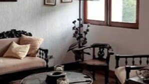 A cozy living room with a sofa, a round coffee table, and a floor lamp. There is a window with a view of greenery outside. - Apartament El Calvario at Casa Ovalle (Antigua Guatemala)
