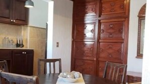A dining area with a wooden table and chairs, a white tablecloth, and a wooden cabinet with decorative panels. - Apartament El Calvario at Casa Ovalle (Antigua Guatemala)