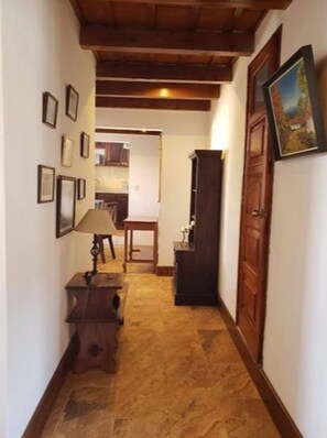 Un estrecho pasillo con suelo de madera, una lámpara y cuadros en las paredes.