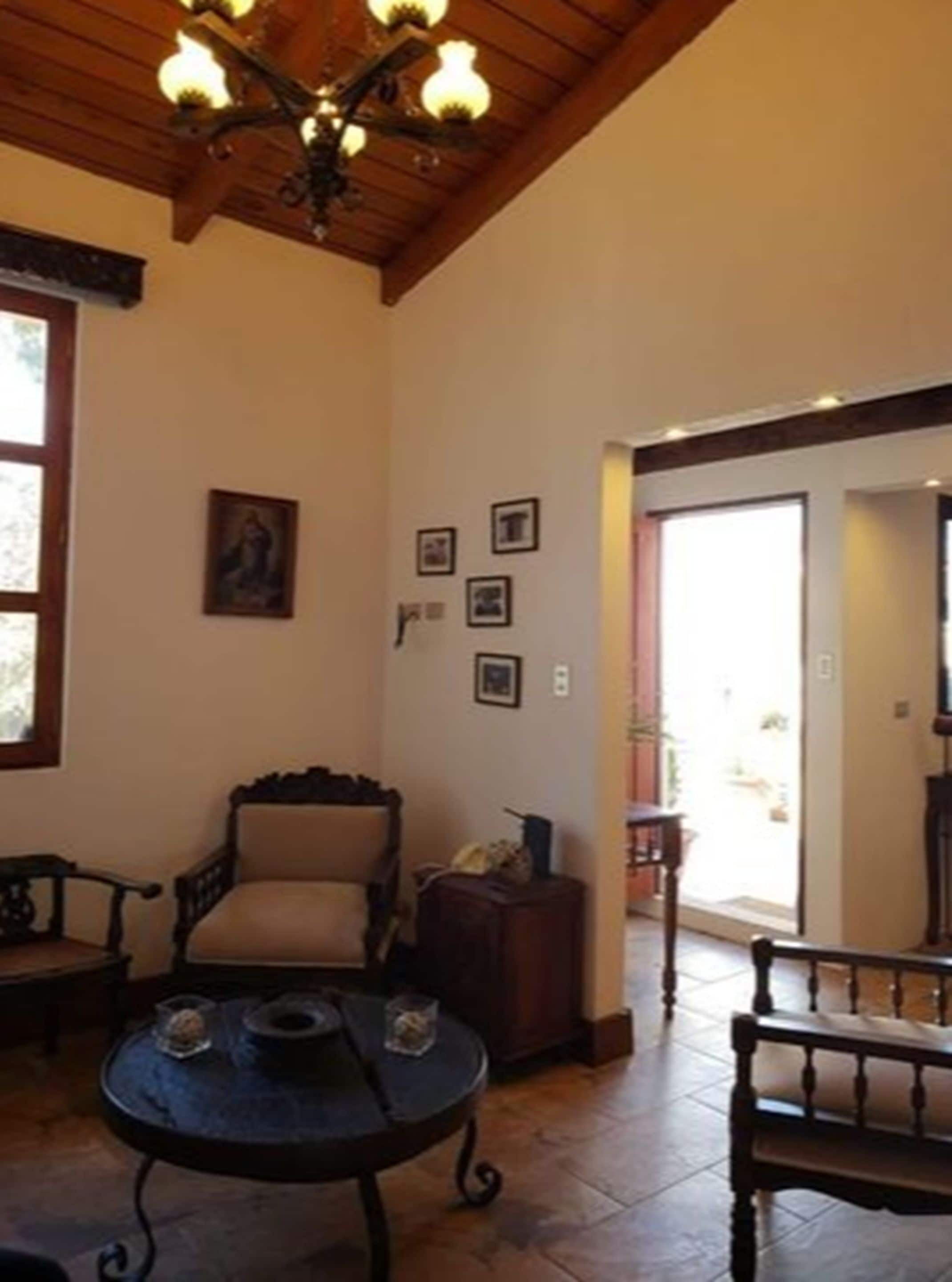 Una habitación con techo de madera, candelabro, ventana grande, sofá, mesa y puerta que da al exterior.