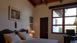 A bedroom with a bed, a wooden headboard, a nightstand with a lamp, a dresser, and a window with a view of the outside. - Apartament El Calvario at Casa Ovalle (Antigua Guatemala)