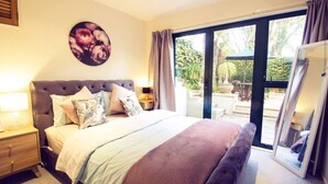 Een slaapkamer met een groot bed, een nachtkastje, een aan de muur hangend schilderij en een schuifdeur die leidt naar een buitenruimte.