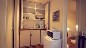 Een praktische keuken met witte kastjes, een magnetron en een broodrooster. Er is een klein aanrecht met een waterkoker en een koffiezetapparaat. Boven het aanrecht hangt een schilderij.