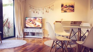Een moderne woonkamer met een houten vloer, witte meubels, een televisie en een eethoek.