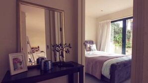 Een slaapkamer met een groot bed, een nachtkastje met spiegel en uitzicht op een balkon.