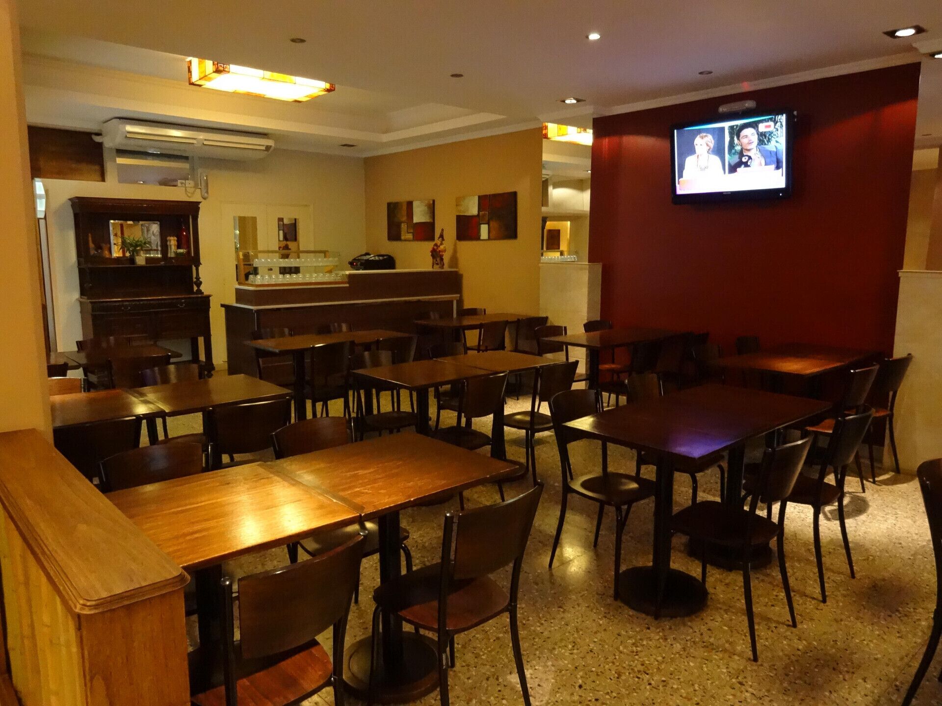A restaurant with multiple tables and chairs, a counter, and a television mounted on the wall.
