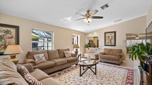 A living room with a beige sofa, a coffee table, and a ceiling fan. - Perfect for big family reunions, sport teams! (Fort Myers)