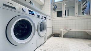 Una lavadora Siemens en un cuarto de lavado bien iluminado, con paredes de azulejos blancos y un banco.