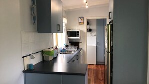 Uma cozinha compacta com bancada preta, micro-ondas, geladeira e pia.