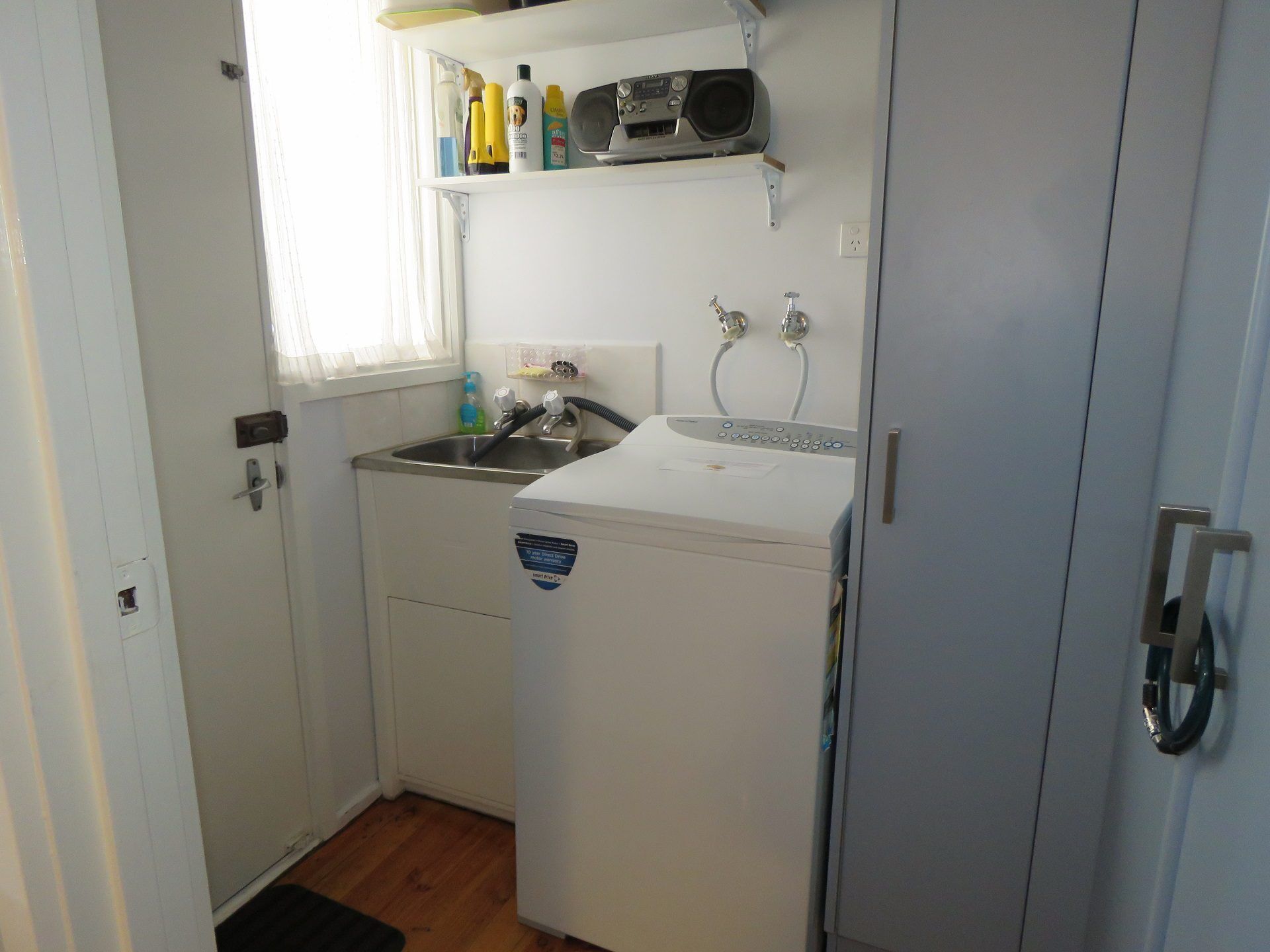 A compact kitchen with a sink, a washing machine, and a shelf with toiletries.