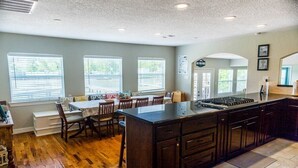 A kitchen with a large island, wooden flooring, and a dining area with chairs and a table.
