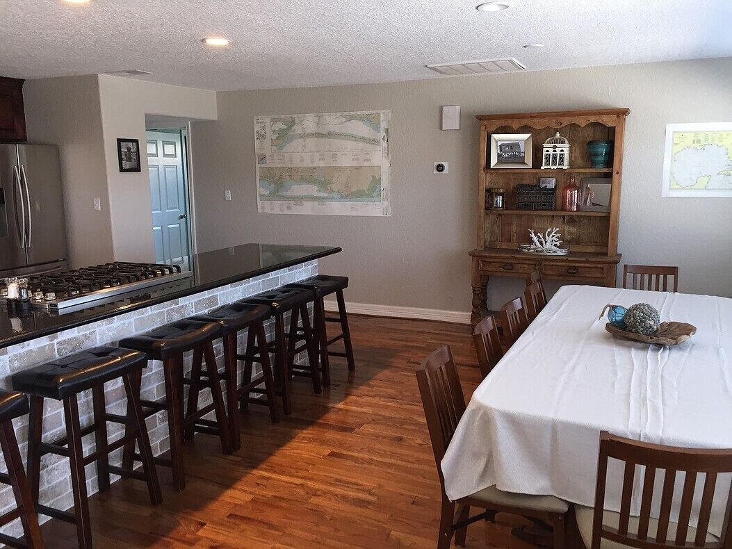 Une cuisine dotée d’un îlot central, de tabourets de bar, d’une table à manger avec des chaises, d’un meuble en bois agrémenté d’objets décoratifs et d’une carte accrochée au mur.