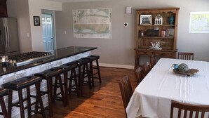 A kitchen with a central island, bar stools, a dining table with chairs, a wooden cabinet with decorative items, and a map on the wall.