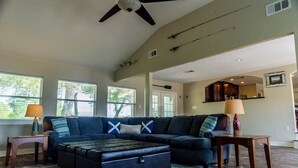 A spacious living room with a sectional sofa, ottoman, and a ceiling fan.