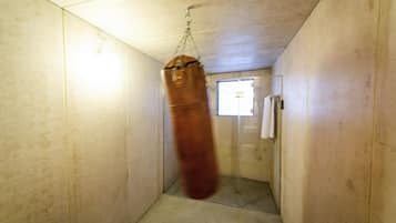 A small, enclosed space with a punching bag hanging from the ceiling, a shower area, and a towel rack on the wall.