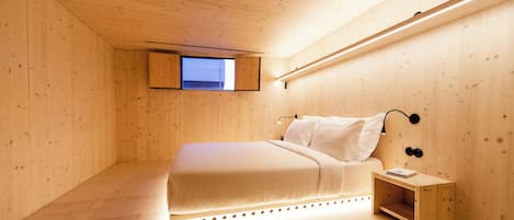 Une pièce aux lignes épurées, avec un décor minimaliste en bois, comprenant un lit, une petite table de chevet et une fenêtre.