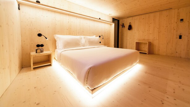 Un dormitorio minimalista de madera con cama, mesita de noche y velador.