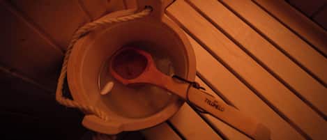 A wooden bucket with a rope handle and a wooden scoop inside, placed on a wooden floor.