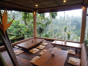 Ein Zimmer mit Holztischen und -bänken, große Fenster mit Blick auf eine tropische Landschaft.