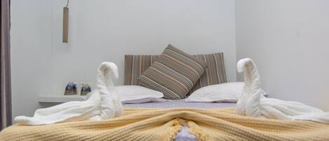 Una cama bien hecha con un almohadón a rayas y uno blanco, una mesita de noche con una lámpara, y un colgante de techo.