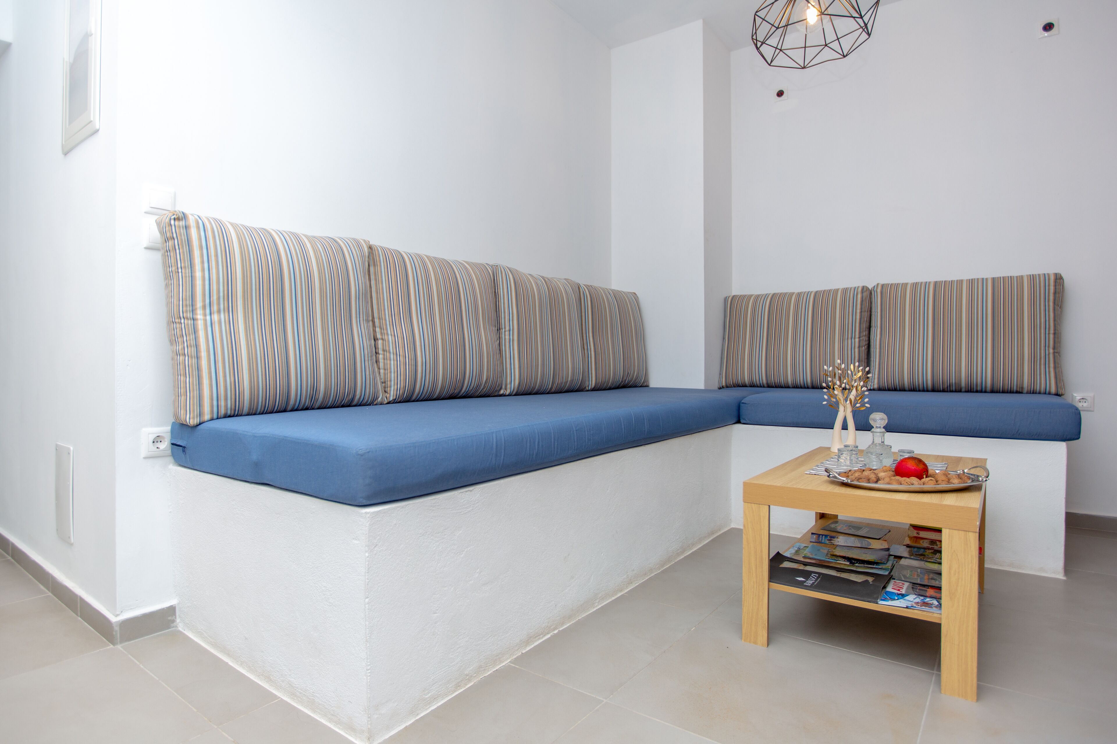 A modern living room with a sectional sofa, a small wooden table with magazines, and a geometric light fixture.