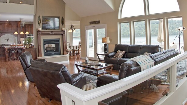 A spacious living area with a high ceiling, a fireplace, a large window, and a staircase leading to an upper level. - Luxurious 5 bedroom, 5+ baths, gourmet kitchen, great location (Camdenton)