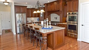A spacious kitchen with wooden cabinets, stainless steel appliances, and a marble island with bar stools. - Luxurious 5 bedroom, 5+ baths, gourmet kitchen, great location (Camdenton)