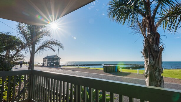 A view from a balcony overlooking a beach with palm trees, a gazebo, and the ocean.