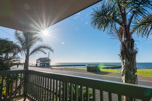 Blick vom Balkon auf einen Strand mit Palmen, einem Pavillon und dem Meer.