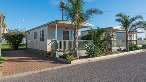 A mobile home with a porch, palm trees, and a paved driveway.