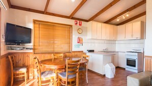 A compact kitchen with wooden cabinets, a built-in stove, and a dining area with a wooden table and chairs.