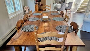 Une salle à manger avec une table en bois dressée pour huit personnes, entourée de chaises dont les assises sont recouvertes d’un tissu tissé.