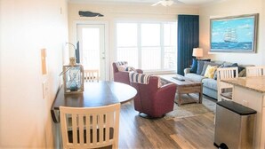 A living room with a dining table, two armchairs, a sofa, a ceiling fan, and a painting of a ship on the wall.