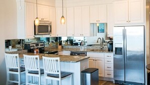 A modern kitchen with white cabinetry, granite countertops, stainless steel appliances, and pendant lighting.