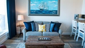 A living room with a sofa, a coffee table, a lamp, and a painting of a ship on the wall.