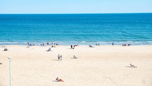 A wide sandy beach with people sunbathing and swimming.
