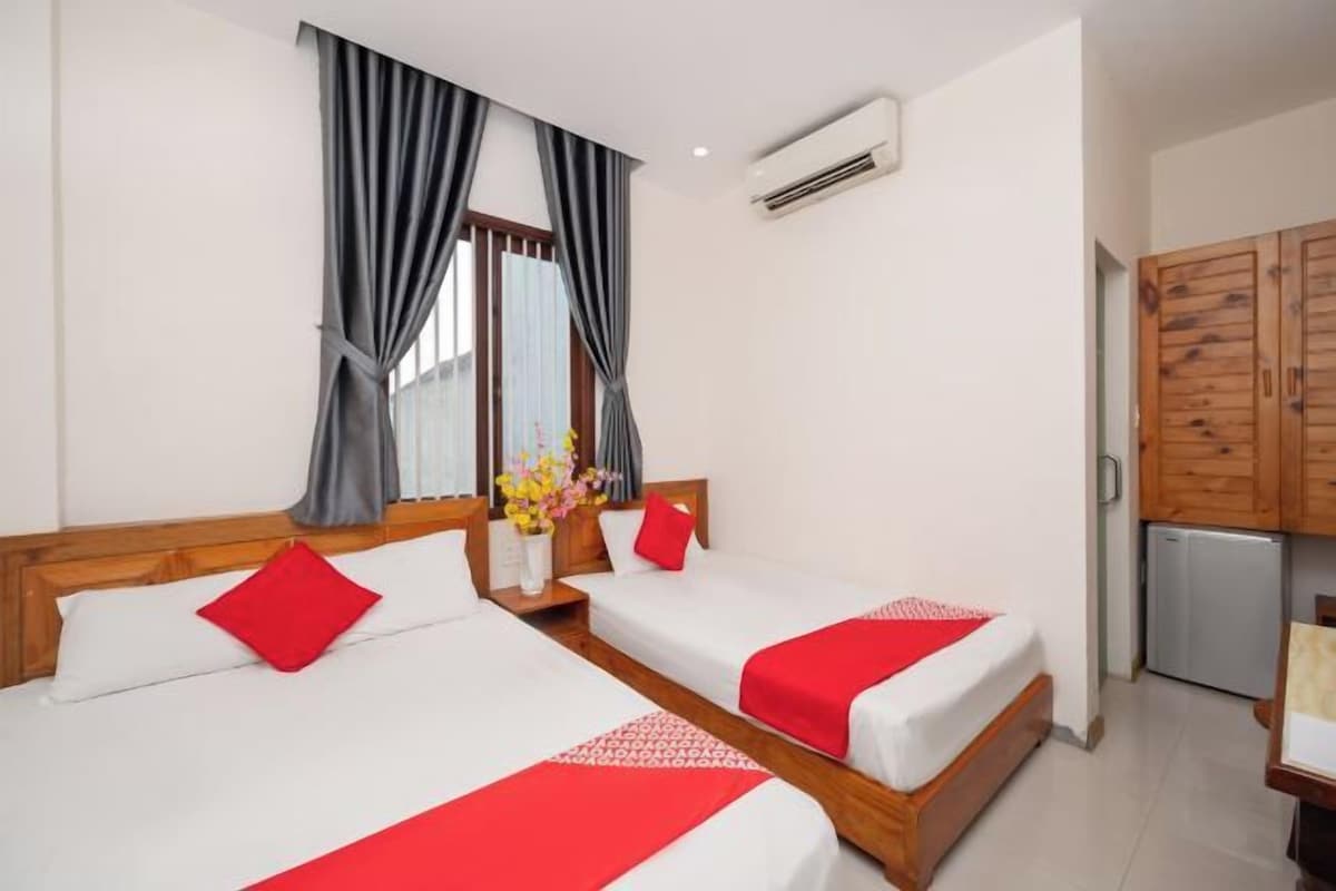 A hotel room with two beds, a wooden wardrobe, a small kitchenette, and an air conditioning unit.