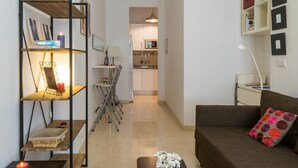 A compact living space with a sofa, a dining table with chairs, a bookshelf, and a kitchen area in the background. - Charming apartment in the Historic Center ideal for couples and families (Málaga)