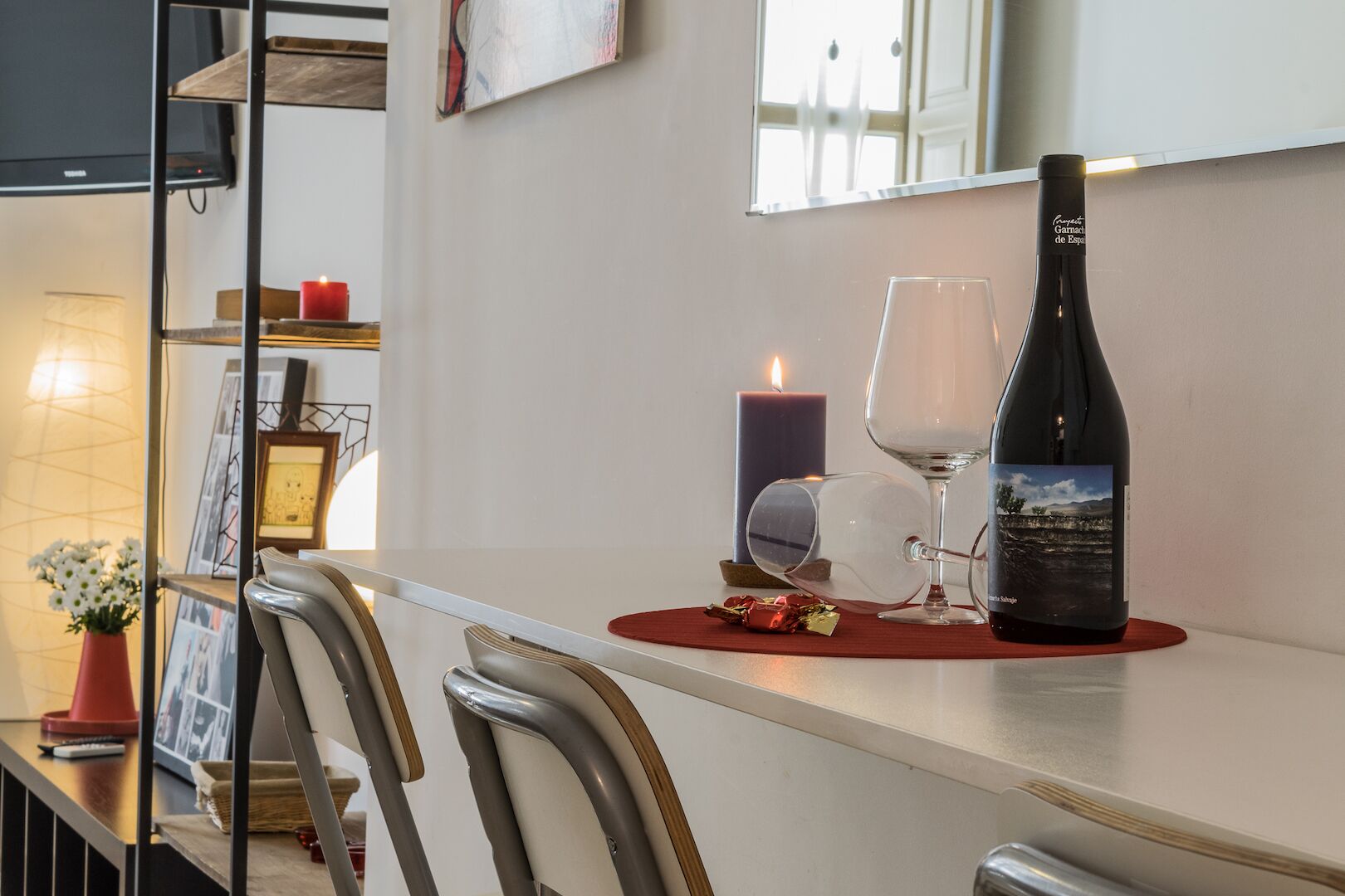 Ein Essbereich mit Tisch für zwei Personen, komplett mit einer Weinflasche, zwei Weingläsern, einer Kerze und einer Vase mit Blumen.