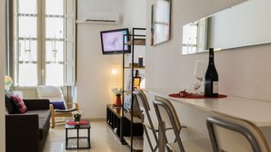A modern living room with a sofa, a small table with a vase, and a TV mounted on the wall. - Charming apartment in the Historic Center ideal for couples and families (Málaga)