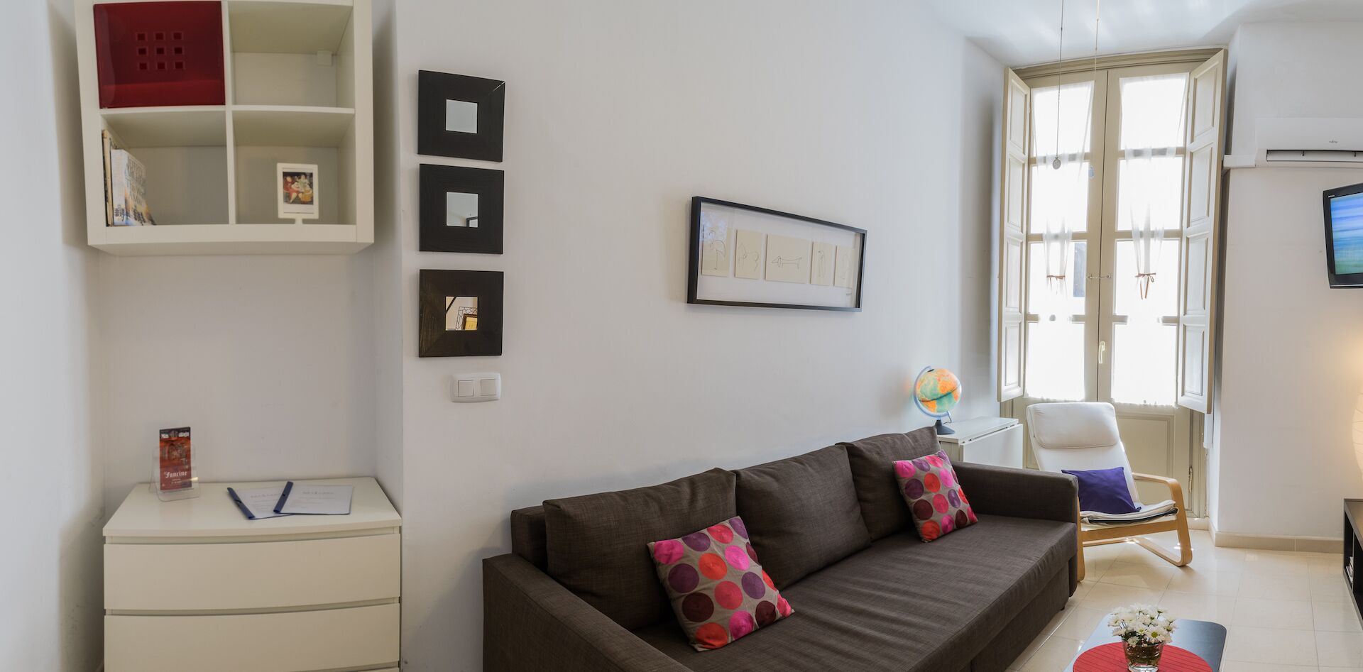 Een woonkamer met een bank, een klein tafeltje met een wereldbol, een stoel en een televisie aan de muur.