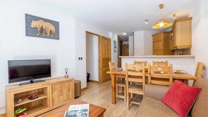Ein gemütliches Wohnzimmer mit Fernseher, Holzmöbeln, einem Essbereich mit Stühlen und einer Küche mit Holzausstattung.