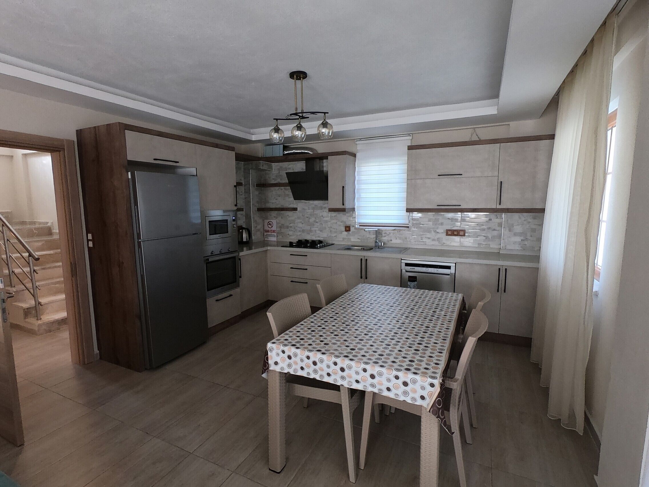 Uma cozinha compacta com geladeira, forno, micro-ondas e pia. Há uma mesa de jantar com cadeiras e uma escada que leva a outro cômodo.