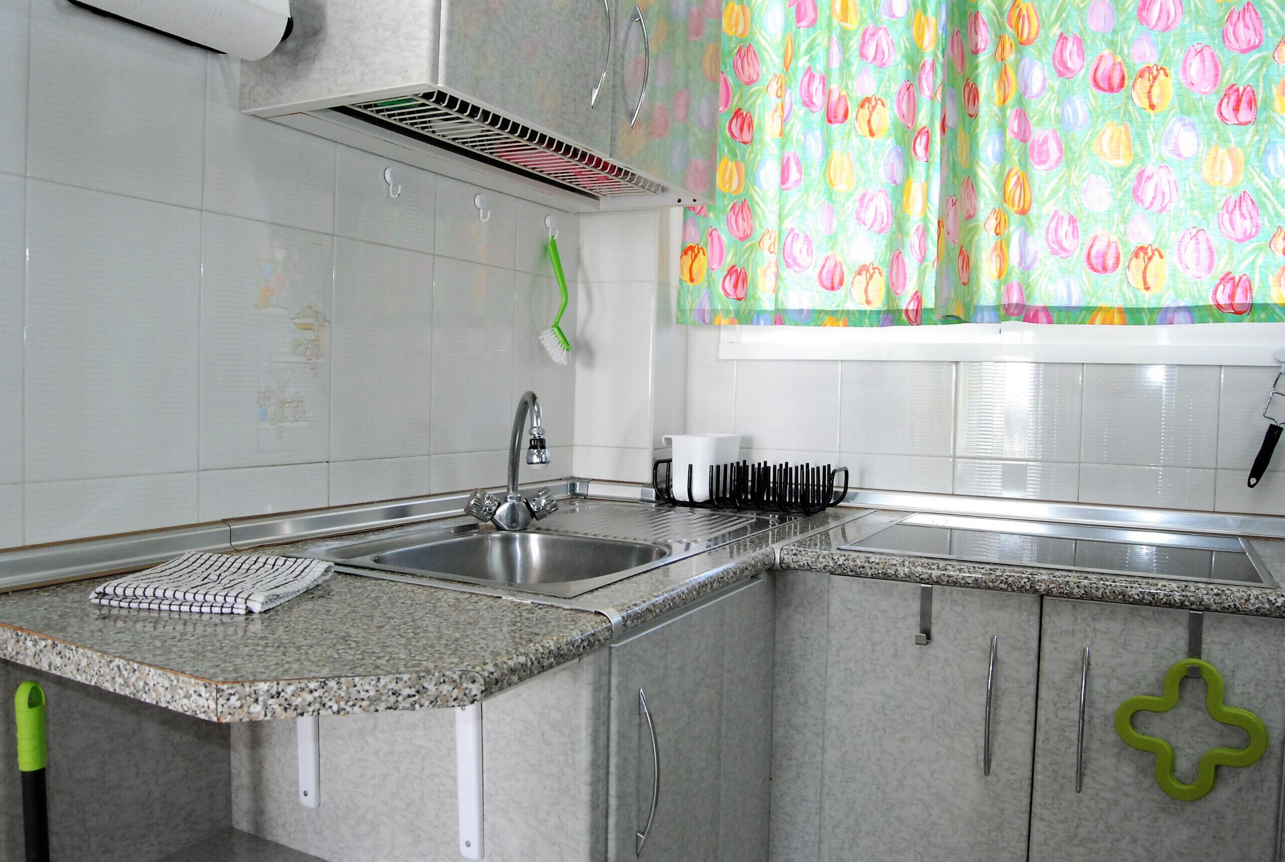 A kitchen with a granite countertop, stainless steel sink, and white tiled backsplash.